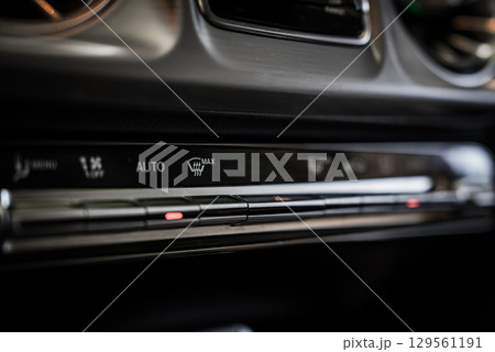 Detailed view of the climate control panel in a Mercedes AMG G Class, featuring metallic buttons, illuminated indicators, and air vents in the background. 129561191