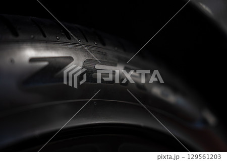 Close up view of a car tire showing ZERO branding on the sidewall, with visible tread grooves and rubber texture against a dark background. 129561203