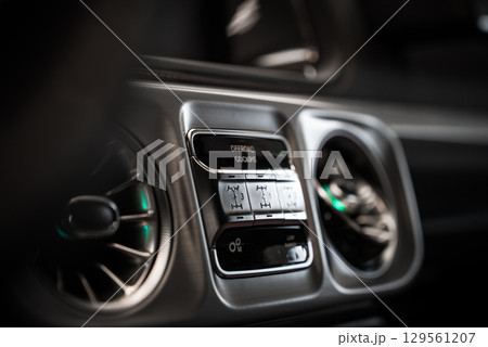 Interior view of Mercedes AMG G Class dashboard, showing brushed metal controls, turbine style air vents, and off road settings in detail. 129561207