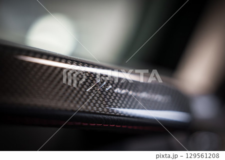 Close up view of a Mercedes Benz AMG carbon fiber interior detail, featuring glossy texture, red stitching accents, and blurred vehicle background. 129561208