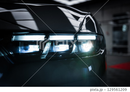 Detailed view of the Ford Mustang GT 5.0 headlight with sharp design and LED elements, reflecting a showroom with bright lights and red carpet. Detailed view of the Ford Mustang GT 5.0 headlight with sharp design and LED elements, reflecting a showroom with bright lights and red carpet. 129561209