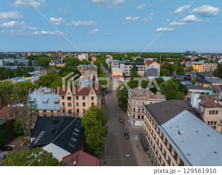 Aerial view of a Riga street lined with historic buildings in Jugendstil style, flanked by green trees, with a skyline of modern and older structures. Aerial view of a Riga street lined with historic buildings in Jugendstil style, flanked by green trees, with a skyline of modern and older structures. 129561910