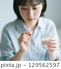 薬をつまんで飲もうとしている日本人女性 129562597