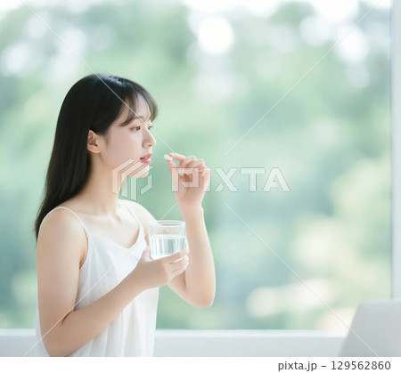 薬をつまんで飲もうとしている日本人女性 129562860