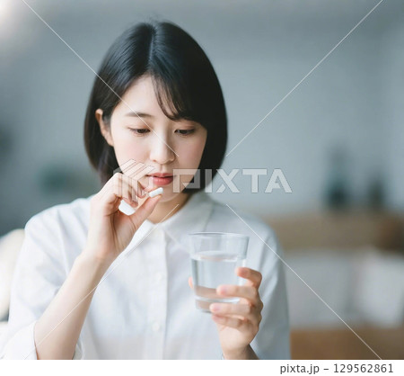 薬をつまんで飲もうとしている日本人女性 129562861