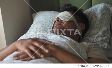 Person resting in bed with sleep mask on Person resting in bed with sleep mask on 129562907