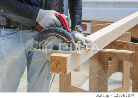 大工さんが丸ノコ用角度切り定規と丸ノコを使って木材を切断している　アップ 129563874