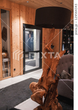 Interior of a luxury hotel in the Italian Alps featuring a sculptural wooden lamp, wood paneling, a wine display, and a modern staircase in the background. Interior of a luxury hotel in the Italian Alps featuring a sculptural wooden lamp, wood paneling, a wine display, and a modern staircase in the background. 129564343