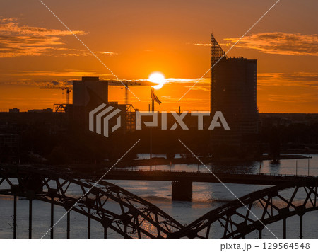 The Riga TV Tower and city skyline stand out at sunset, with the Daugava River and a bridge in the foreground. A Latvian flag is visible near the center. The Riga TV Tower and city skyline stand out at sunset, with the Daugava River and a bridge in the foreground. A Latvian flag is visible near the center. 129564548