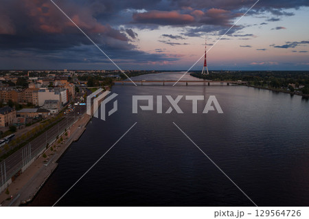 Riga, Latvia at sunset with the Daugava River, Riga TV Tower on the right, a bridge in the midground, and urban architecture along the riverbank. Riga, Latvia at sunset with the Daugava River, Riga TV Tower on the right, a bridge in the midground, and urban architecture along the riverbank. 129564726