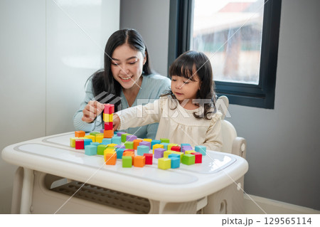 happy toddler girl playing wooden block toy cubes with her mother on table happy toddler girl playing wooden block toy cubes with her mother on table 129565114