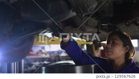 Image of mid adult female asian mechanic draining engine oil from car in garage 129567626