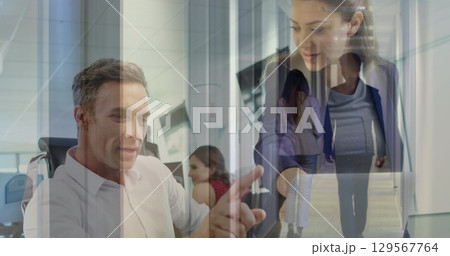 Image of coworkers discussing over laptop in office and colleagues walking in corridor Image of coworkers discussing over laptop in office and colleagues walking in corridor 129567764