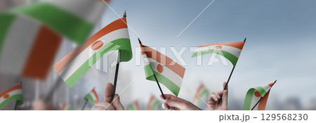 Niger flags in their hands on a blurred urban background 129568230