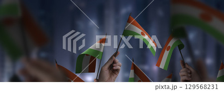 Niger flags in their hands on a blurred urban background Niger flags in their hands on a blurred urban background 129568231