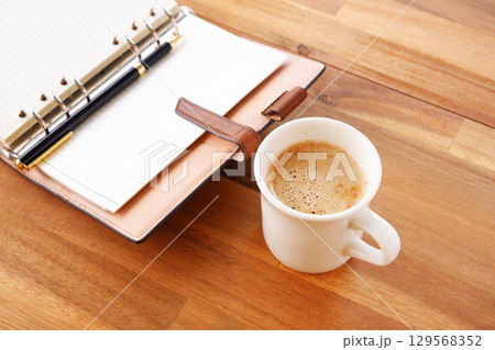 ミルクをたっぷり入れたコーヒー、カフェ・ラッテを飲みながら、システム手帳でデスクワーク中のイメージ ミルクをたっぷり入れたコーヒー、カフェ・ラッテを飲みながら、システム手帳でデスクワーク中のイメージ 129568352