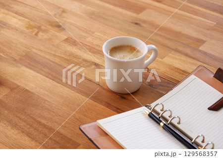 ミルクをたっぷり入れたコーヒー、カフェ・ラッテを飲みながら、システム手帳でデスクワーク中のイメージ 129568357