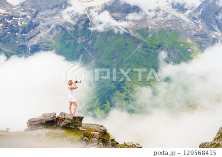 Young Woman Captures Majestic Grossglockner, Austria Views with Camera Above the Clouds 129568415