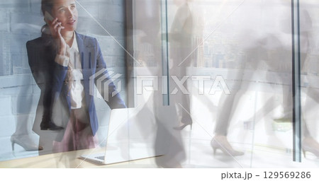 Image of caucasian businesswoman talking on smartphone over time lapse of people and skyscrapers 129569286