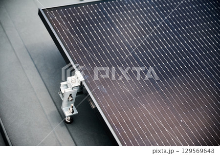 Close up of solar panel, securely fastened with robust mounting clamp to supporting structure on rooftop of house. Bolts and clamps provide stability and durability to solar installation. Close up of solar panel, securely fastened with robust mounting clamp to supporting structure on rooftop of house. Bolts and clamps provide stability and durability to solar installation. 129569648