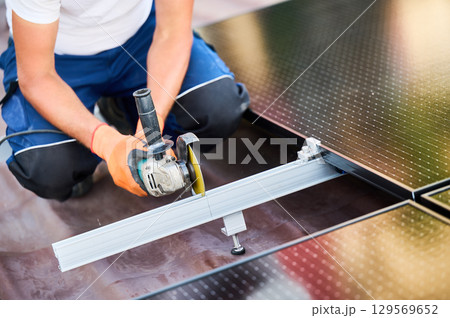 Worker installing or maintaining photovoltaic solar panel system on roof of house. Close up technician using grinder on metal part of the panel's mounting structure. Concept renewable energy. 129569652