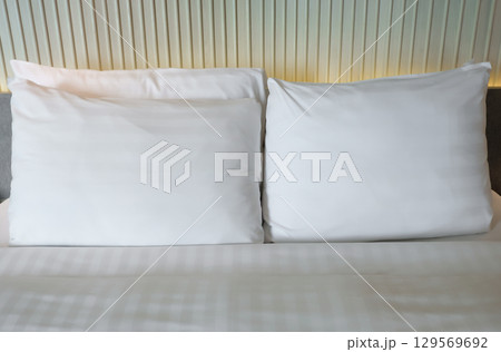 Two white pillows on a bed with a textured headboard backdrop. Two white pillows on a bed with a textured headboard backdrop. 129569692