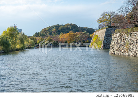 Tranquil river scene with autumn foliage and stone wall of Himeji Castle Japan 129569983