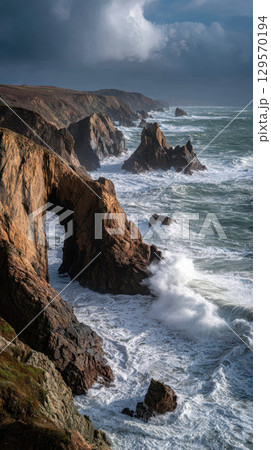 Dramatic rocky coastline with natural arch, crashing waves, and moody sky, remote and wild 129570194