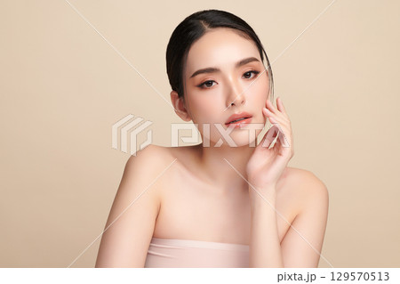 A beautiful young Asian woman with clean, fresh skin against a beige background. Skincare, facial treatment, cosmetology, beauty, and spa. An elegant portrait of an Asian woman. 129570513