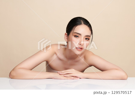 A beautiful young Asian woman with clean, fresh skin against a beige background. Skincare, facial treatment, cosmetology, beauty, and spa. An elegant portrait of an Asian woman. 129570517