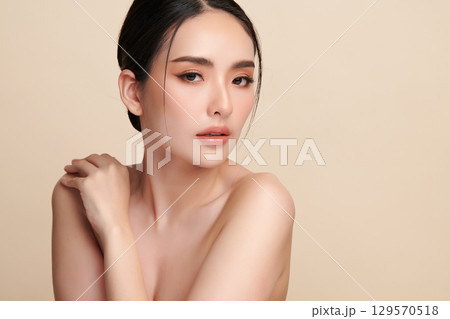 A beautiful young Asian woman with clean, fresh skin against a beige background. Skincare, facial treatment, cosmetology, beauty, and spa. An elegant portrait of an Asian woman. 129570518