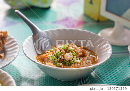 Spicy meat and tomato dip on white plate on wooden table, Nam Prik Aong, Northen Thai food 129571359