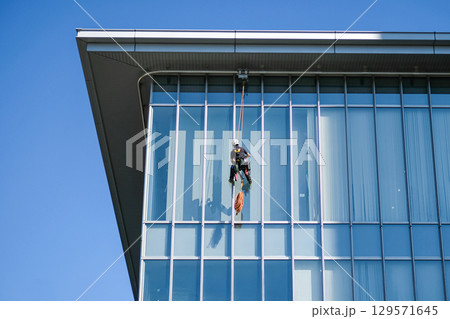 Worker cleaning glass building facade 129571645
