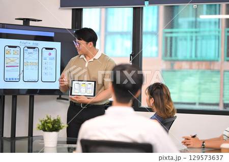 Creative team exchanging ideas on adaptive interface design, with hand drawn wireframes on a large screen 129573637