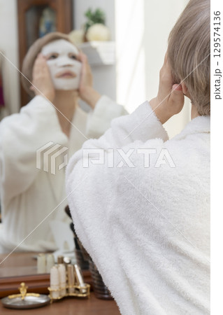 鏡の前でフェイスマスクで肌ケアをするシニア女性 129574136
