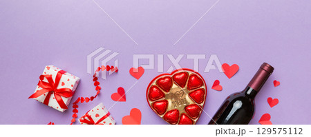 Bottle of red wine on colored background for Valentine Day with gift and chocolate. Heart shaped with gift box of chocolates top view with copy space Bottle of red wine on colored background for Valentine Day with gift and chocolate. Heart shaped with gift box of chocolates top view with copy space 129575112