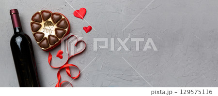 Bottle of red wine on colored background for Valentine Day with gift and chocolate. Heart shaped with gift box of chocolates top view with copy space Bottle of red wine on colored background for Valentine Day with gift and chocolate. Heart shaped with gift box of chocolates top view with copy space 129575116