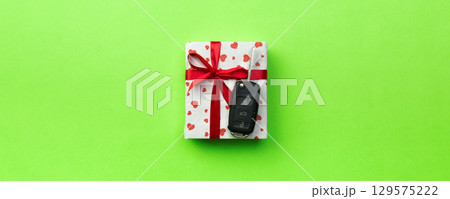 Give gift car key concept top view. Present box with red ribbon bow, heart and car key on green colored background 129575222