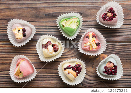 chocolate sweets in the form of a heart with fruits and nuts on a colored background. top view with space for text, holiday concept chocolate sweets in the form of a heart with fruits and nuts on a colored background. top view with space for text, holiday concept 129575251