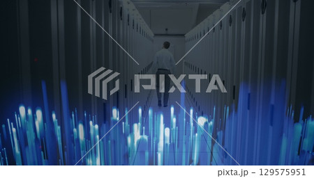Image of glowing blue light trails over rear view of male engineer walking in server room 129575951