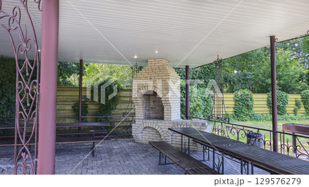 A tall brick oven in a gazebo in nature for cooking food on fire and skewers. 129576279