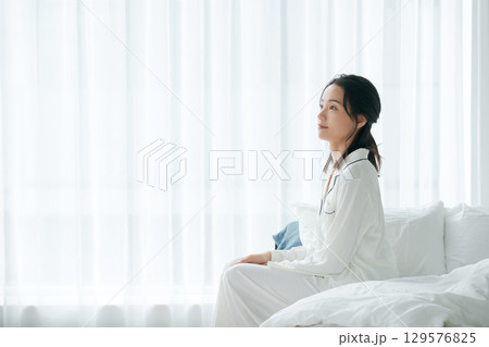 朝起きてベッドに座る疲れた表情の女性 129576825