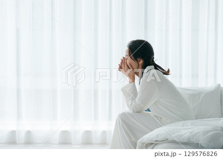 朝起きてベッドに座るパジャマの女性 129576826