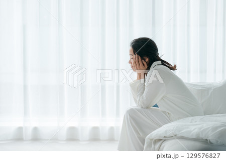 朝起きてベッドに座るパジャマの女性 129576827