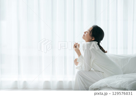 朝起きてベッドに座るパジャマの女性 朝起きてベッドに座るパジャマの女性 129576831
