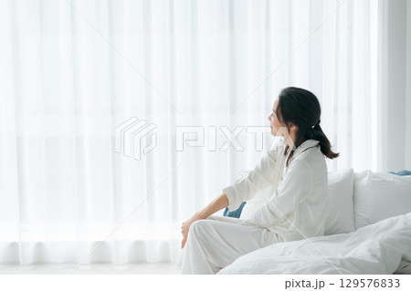 朝起きてベッドに座るパジャマの女性 129576833
