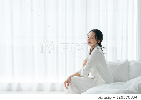 朝起きてベッドに座るパジャマの女性 129576834