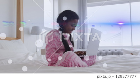 Image of light spots and trails over african american girl using laptop Image of light spots and trails over african american girl using laptop 129577777