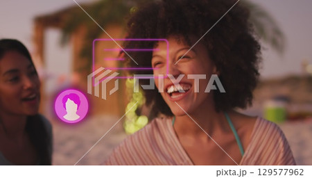 Image of profile icon with speech bubble over two diverse female friends smiling at the beach 129577962