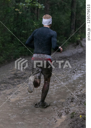 Athlete running puddles of mud in heavy rain during forest marathon 129579018
